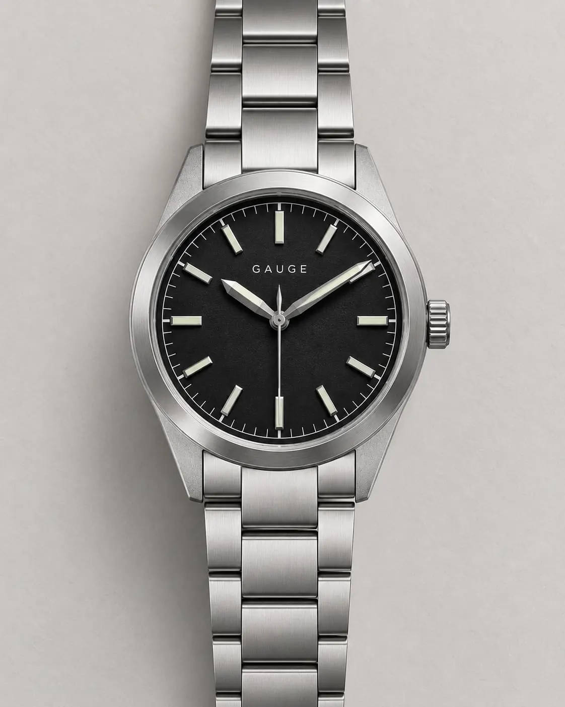 GAUGE-01 Field, black dial, steel bracelet, front-on on a warm-grey ground steel plate.