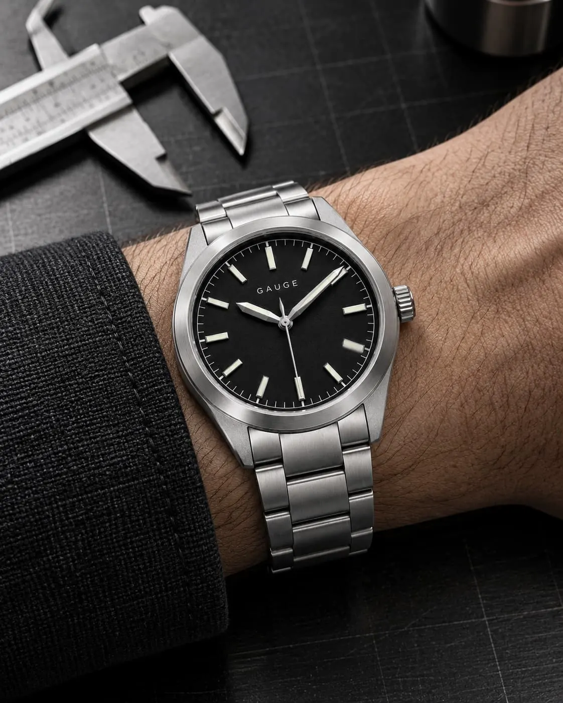 GAUGE-01 Field on a wrist with a dark cuff, resting on a workbench beside a caliper.