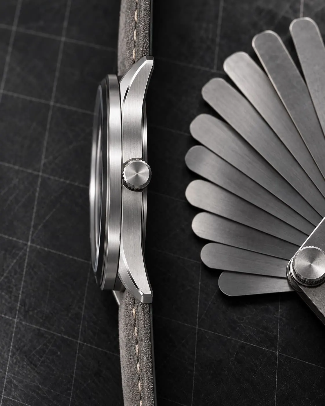 GAUGE-03 Bench in profile on a grey suede strap, beside a fanned set of steel feeler gauges.